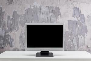 Modern minimalistic workspace featuring a blank computer monitor against a textured gray wall photo