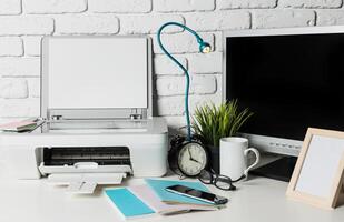 Workspace essentials showcasing printer, monitor, clock, and desk items in a modern office setting photo