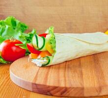 Fresh vegetable wrap with lettuce, tomato, and cucumber on a wooden cutting board photo