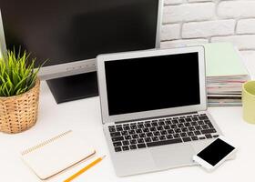 Workspace setup featuring laptop, monitor, and stationery with greenery in a modern office environment photo