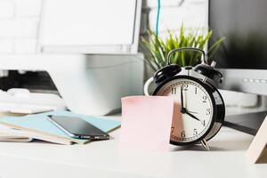 Office desk setup featuring an alarm clock, smartphone, and sticky notes during a productive workday photo