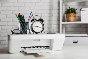 Desk setup with a printer, clock, and office supplies in a modern workspace during the day photo