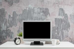 Modern workspace design with a computer, clock, and coffee cup against a textured gray backdrop photo