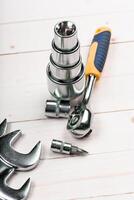 Various hand tools including sockets and a ratchet wrench arranged on a wooden surface photo