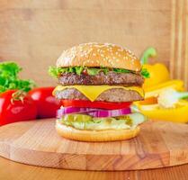 Delicious double cheeseburger on a wooden cutting board with fresh vegetables at a casual dining setting photo