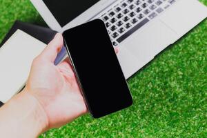 Displaying a smartphone above a laptop on green turf in a cozy workspace setting photo
