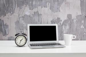 Desk setup with a laptop, alarm clock, and coffee cup in a modern workspace setting photo