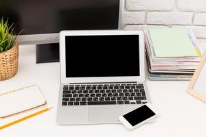 Workspace featuring a laptop and smartphone with notepad and magazines, set on a clean desk photo