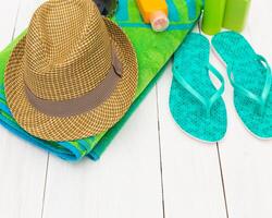 Summer beach essentials including towel, sun hat, sunscreen, and flip flops arranged on a bright wooden surface photo