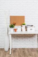 Organized workspace with plants and stationery on a desk against a brick wall backdrop photo