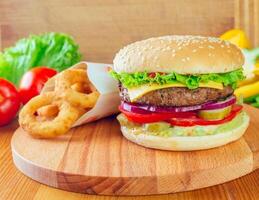 Delicious cheeseburger served with crispy onion rings and fresh vegetables on a wooden board photo