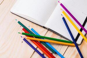 Colorful pencils scattered beside an open notebook on a wooden surface create a vibrant study space photo