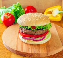 Juicy handmade burger topped with fresh vegetables served on a wooden board in natural light photo