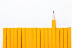 Yellow pencils arranged in a neat row with one pencil standing out against a white background photo