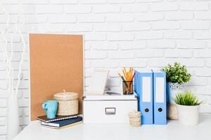 Organized workspace with stationery, greenery, and storage solutions on a white brick backdrop photo