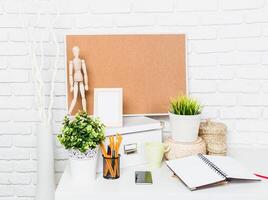 Workspace setup with plants, stationery, and a cork board for organization and creativity in a bright, minimalist design photo