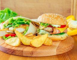 Delicious burger and chicken wrap served with golden fries on a wooden platter in a cozy setting photo