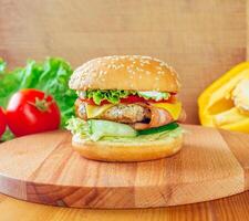 Delicious homemade burger with lettuce, tomato, cheese, and grilled chicken on a wooden chopping board photo