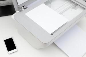 Printer in an office setting with blank paper and smartphone nearby during a workday routine photo