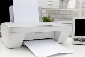 Modern printer printing documents on a white table in a cozy workspace with a laptop and decor photo