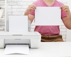 Person using a printer in a bright workspace, holding printed paper and blank page during a home office activity photo