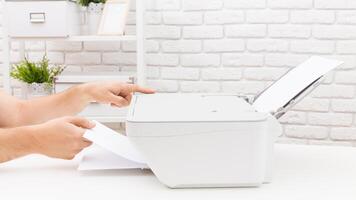 Person preparing documents for printing in a bright office setting with white brick walls and shelves of plants photo