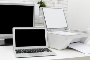 Home office setup with laptop printer and monitor in a modern workspace during daylight hours photo