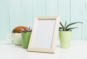 Decorative empty frame with succulent plants and a cactus on a white table against a light blue wooden backdrop photo