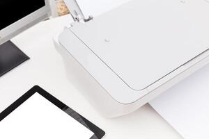 Printer and tablet on a workspace with clean papers and computer monitor in a bright setting photo