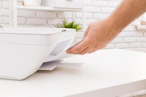 Hand retrieving printed document from a white printer in a modern workspace photo