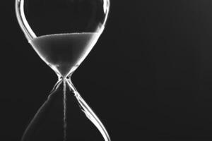 Vintage hourglass filled with sand captures the essence of time flowing quietly in minimalist black and white setting photo