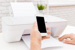 Person using smartphone to print document from home printer in bright workspace during the day photo