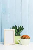 Decorative indoor setup featuring vibrant plants and a blank picture frame against a blue wooden background photo