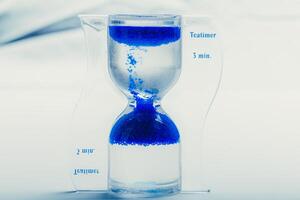 Unique hourglass timer with blue sand indicating three minutes for brewing tea photo