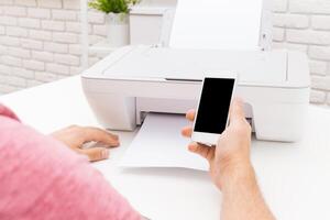 Person using smartphone to print document from printer in modern workspace photo