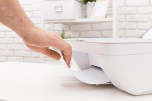 Hand reaching to retrieve printed document from modern printer on a clean desk in a bright workspace photo
