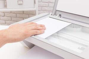 Hands placing paper in a multifunction printer for scanning in a modern workspace photo