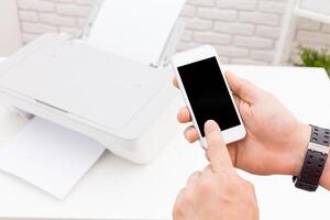 Hands holding a smartphone to print documents wirelessly from a mobile device in a modern office setting photo