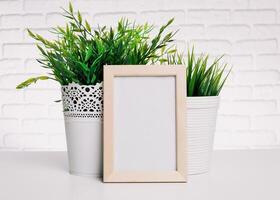 Indoor decoration with artificial plants and a blank frame on a minimalist table against a textured white wall photo