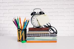 Organized workspace featuring stationery, an alarm clock, and colorful pencils on a white brick backdrop in a bright environment photo