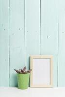 Decorative setup featuring a green pot with a succulent and an empty picture frame against a light blue wooden background photo