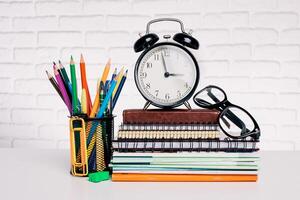 Colorful stationery and clock on a desk with stacked notebooks and glasses in a bright workspace photo