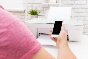 Person printing documents from smartphone while seated at modern desk in bright workspace photo