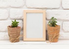 Decorative plants in woven pots with a blank frame on a white brick wall shelf photo