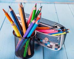 Colorful pencils in a black holder next to a pencil case on a blue wooden surface photo