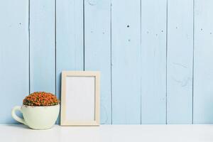 Decorative setup with a flower pot and empty frame against a pastel blue wooden wall photo