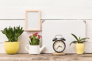 Decorative indoor plants with clock and empty frame on wooden table in cozy living space photo