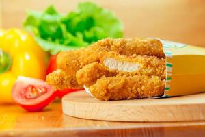 Crispy fried chicken tenders served with fresh vegetables on a wooden board photo