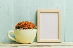 Decorative arrangement featuring a plant in a cup beside an empty frame on a wooden surface photo