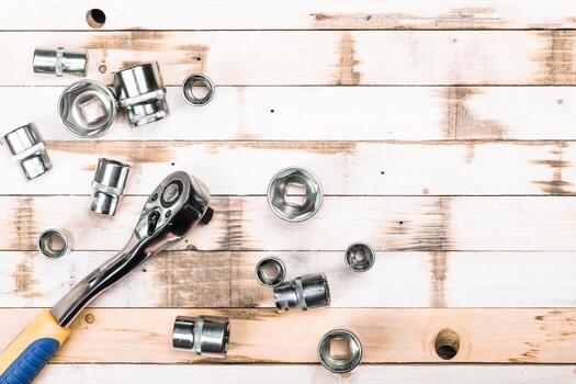Tools scattered on a wooden workbench with a ratchet wrench and various socket sizes in a workshop setting photo